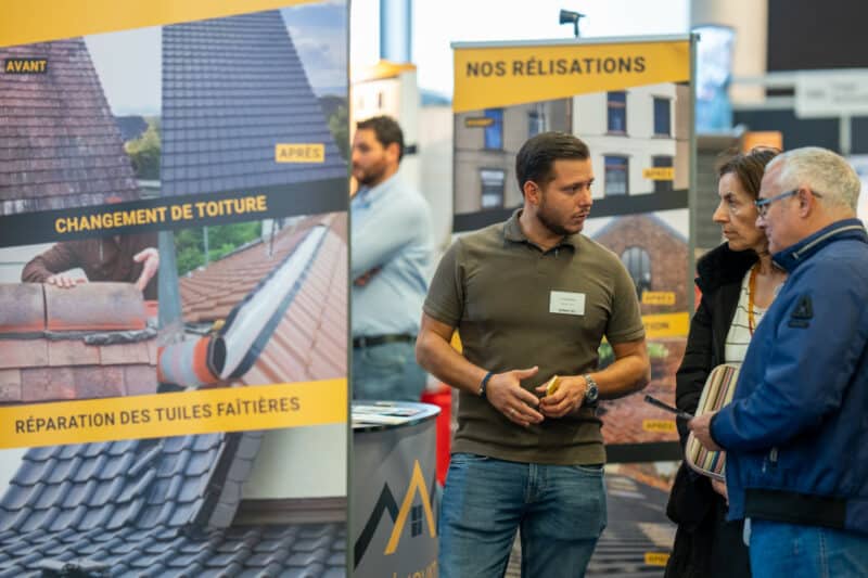 Exposant en toiture présentant ses réalisations à des visiteurs sur son stand au salon Batireno